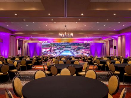A large conference room with round tables and chairs, a colorful backdrop, and purple lighting creating a vibrant atmosphere, ending the sentence.