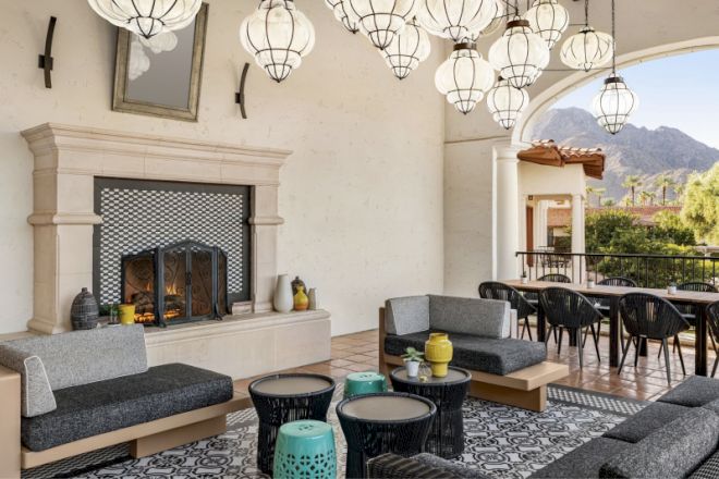 An outdoor lounge with modern furniture, lantern-style lighting, a fireplace, and a dining area in a picturesque setting with mountain views.