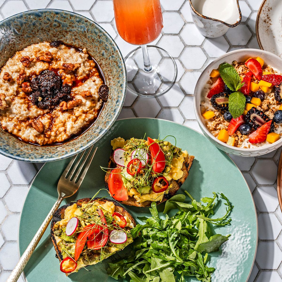 The image shows a variety of breakfast items including avocado toast, grilled grapefruit, oatmeal, a bowl of fruit, coffee, and a tall beverage.