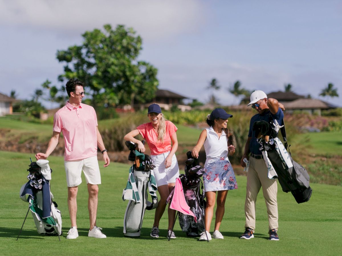Four people on a golf course are carrying golf bags and equipment, dressed in casual golfing attire, and appear to be enjoying their day.