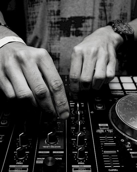 A black and white photo of someone using DJ equipment, adjusting controls on a console with two turntables and various buttons.