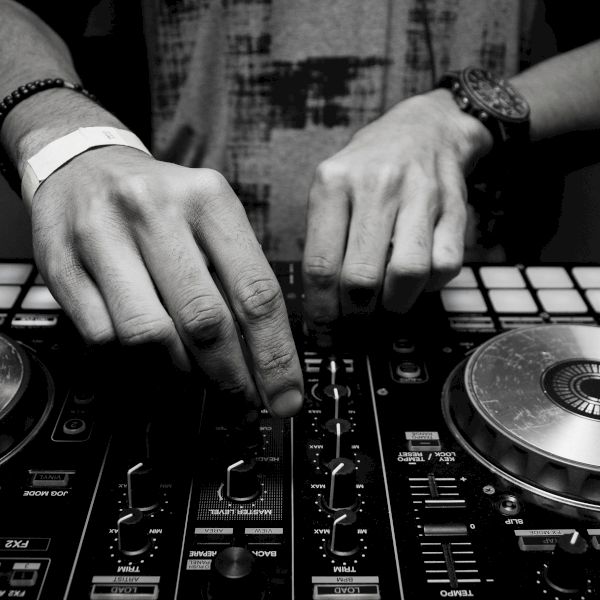 A black and white photo of someone using DJ equipment, adjusting controls on a console with two turntables and various buttons.